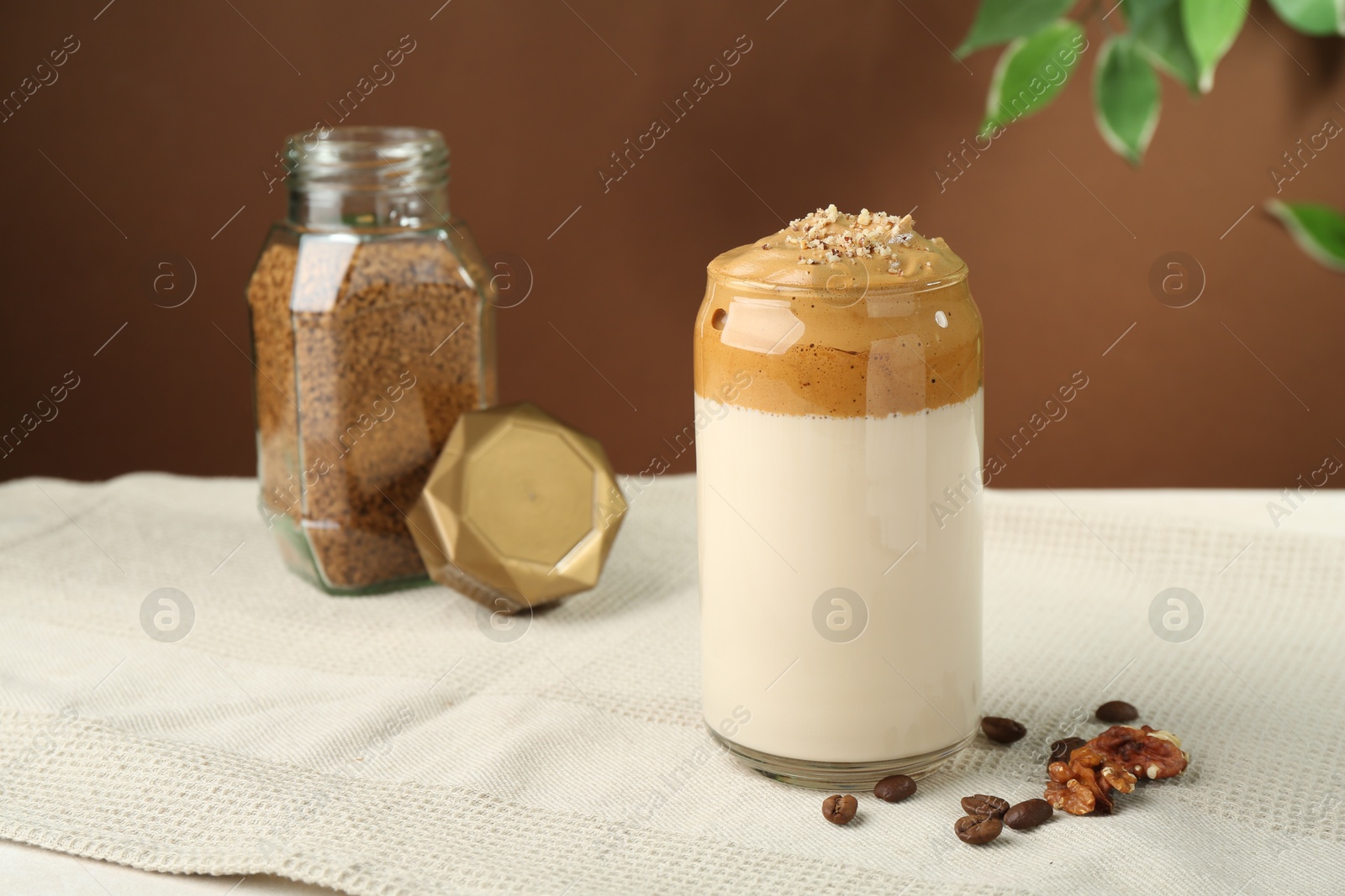 Photo of Delicious dalgona coffee in glass, beans, walnuts and granules on table