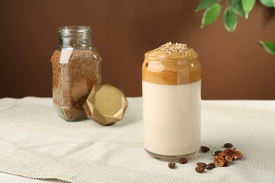 Photo of Delicious dalgona coffee in glass, beans, walnuts and granules on table