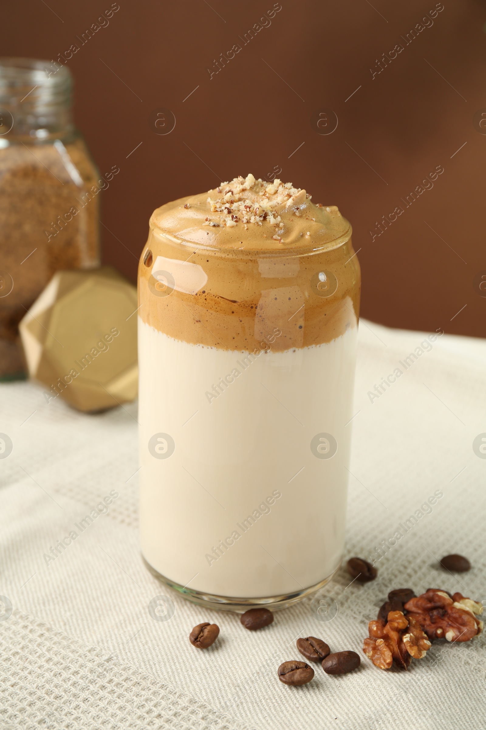 Photo of Delicious dalgona coffee in glass, beans, walnuts and granules on table, closeup