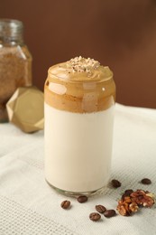 Photo of Delicious dalgona coffee in glass, beans, walnuts and granules on table, closeup