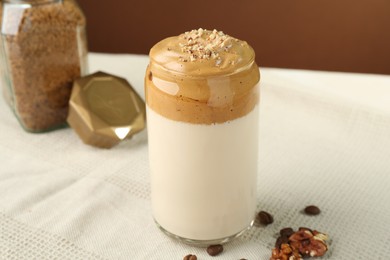Photo of Delicious dalgona coffee in glass, beans, walnuts and granules on table, closeup