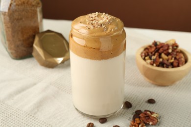 Photo of Delicious dalgona coffee in glass, beans, walnuts and granules on table, closeup