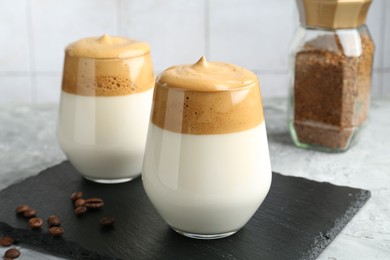 Photo of Delicious dalgona coffee in glasses, beans and granules on grey table, closeup