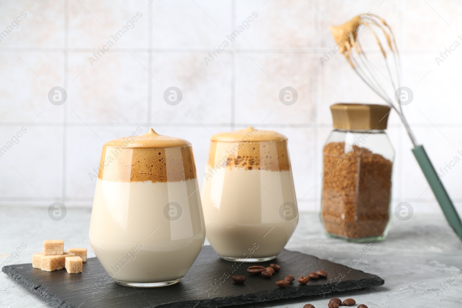 Delicious dalgona coffee in glasses, brown sugar, beans, whisk and granules on grey table, closeup Photo of Delicious dalgona coffee in glasses, brown sugar, beans, whisk and granules on grey table, closeup
