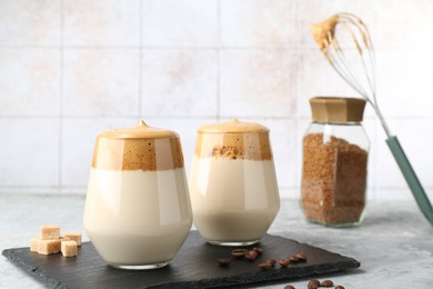 Photo of Delicious dalgona coffee in glasses, brown sugar, beans, whisk and granules on grey table, closeup