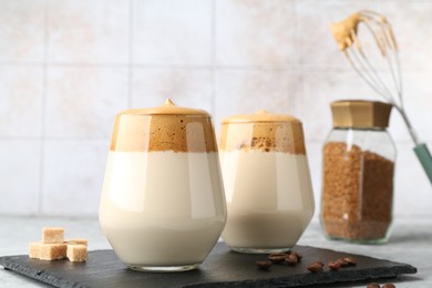 Photo of Delicious dalgona coffee in glasses, brown sugar, beans, granules and whisk on table, closeup