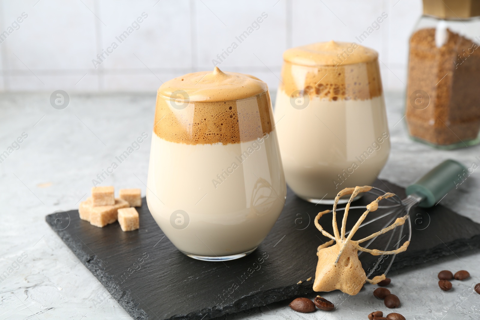 Photo of Delicious dalgona coffee in glasses, brown sugar, beans, whisk and granules on grey table, closeup