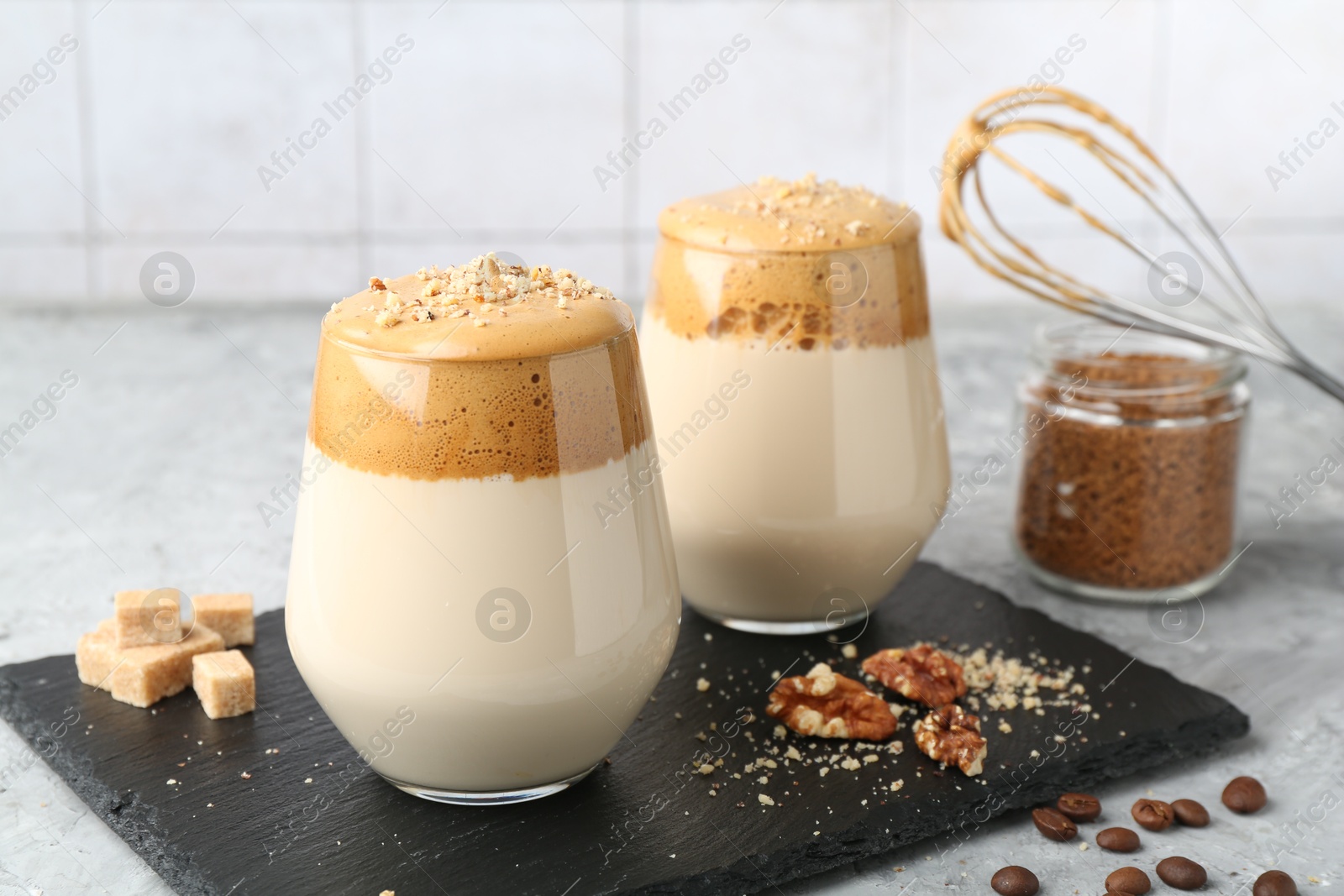 Photo of Delicious dalgona coffee in glasses, brown sugar, beans, walnuts, whisk and granules on grey table, closeup