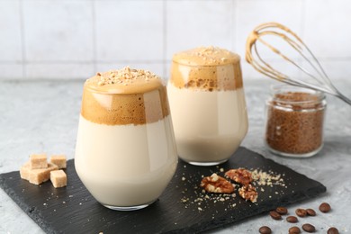 Photo of Delicious dalgona coffee in glasses, brown sugar, beans, walnuts, whisk and granules on grey table, closeup