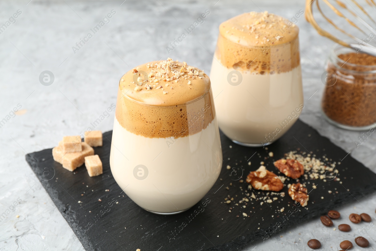 Photo of Delicious dalgona coffee in glasses, brown sugar, beans, walnuts and granules on grey table, closeup