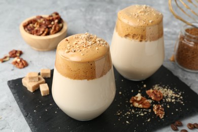 Photo of Delicious dalgona coffee in glasses, brown sugar, beans, walnuts and granules on grey table, closeup
