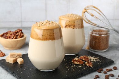 Photo of Delicious dalgona coffee in glasses, brown sugar, beans, walnuts, whisk and granules on grey table, closeup