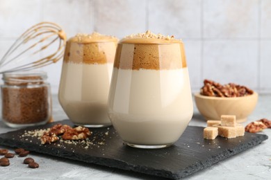 Photo of Delicious dalgona coffee in glasses, brown sugar, beans, walnuts, whisk and granules on grey table, closeup
