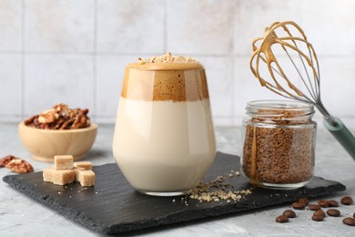 Photo of Delicious dalgona coffee in glass, brown sugar, beans, walnuts, whisk and granules on grey table, closeup