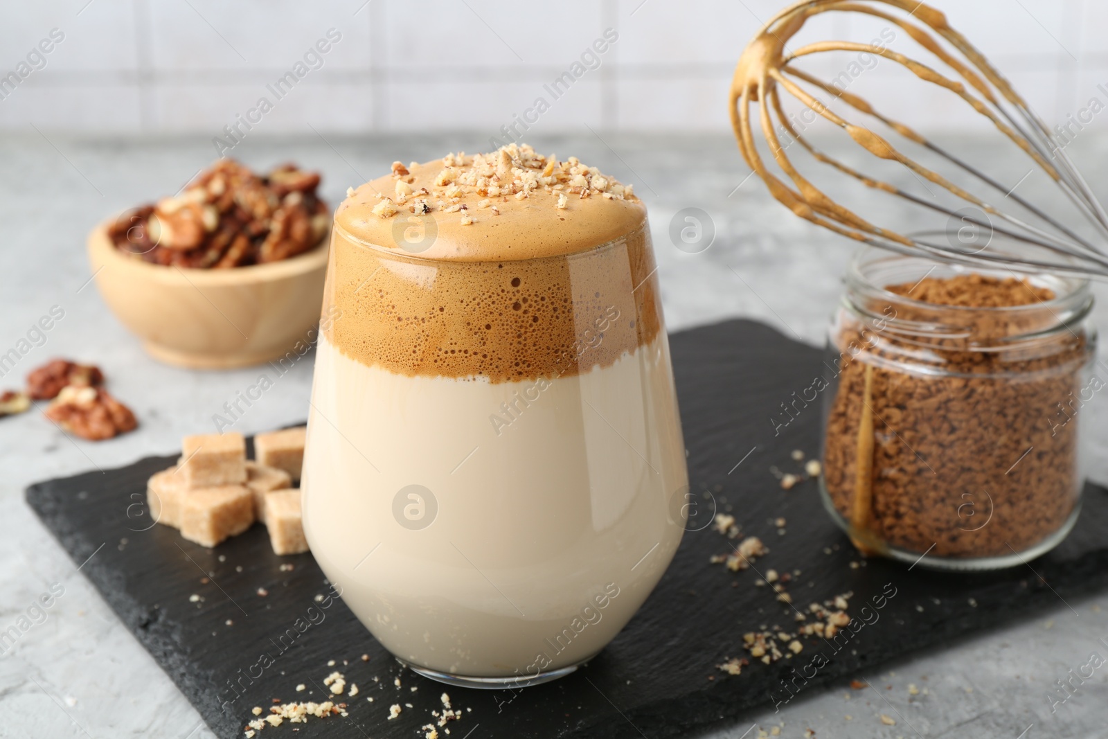 Delicious dalgona coffee in glass, brown sugar, walnuts, whisk and granules on grey table, closeup Photo of Delicious dalgona coffee in glass, brown sugar, walnuts, whisk and granules on grey table, closeup