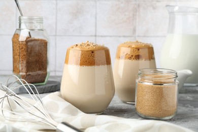 Photo of Delicious dalgona coffee in glasses, whisk, brown sugar and granules on grey table