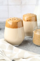 Photo of Delicious dalgona coffee in glasses and brown sugar on grey table, closeup