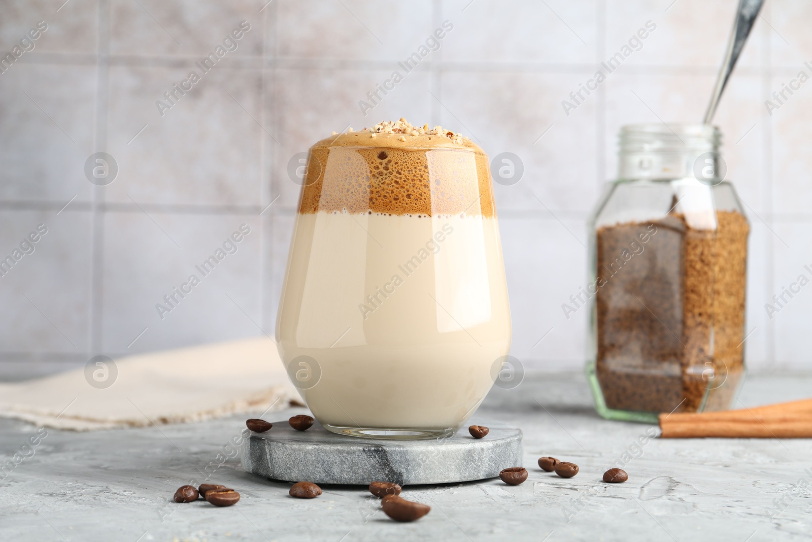 Delicious dalgona coffee in glass, beans, granules and cinnamon on grey table Photo of Delicious dalgona coffee in glass, beans, granules and cinnamon on grey table