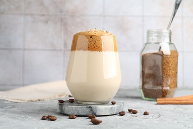 Photo of Delicious dalgona coffee in glass, beans, granules and cinnamon on grey table