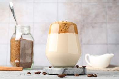 Photo of Delicious dalgona coffee in glass, beans, granules and cinnamon on grey table, low angle view
