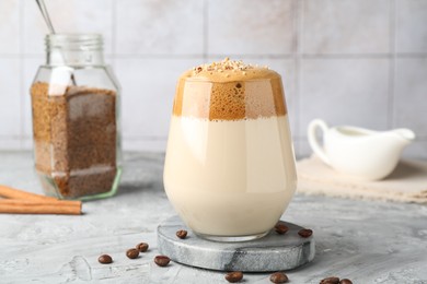 Photo of Delicious dalgona coffee in glass, beans, granules and cinnamon on grey table, closeup
