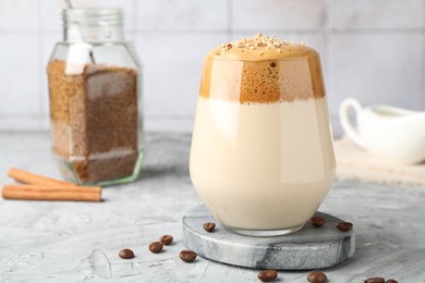 Photo of Delicious dalgona coffee in glass, beans, granules and cinnamon on grey table, closeup
