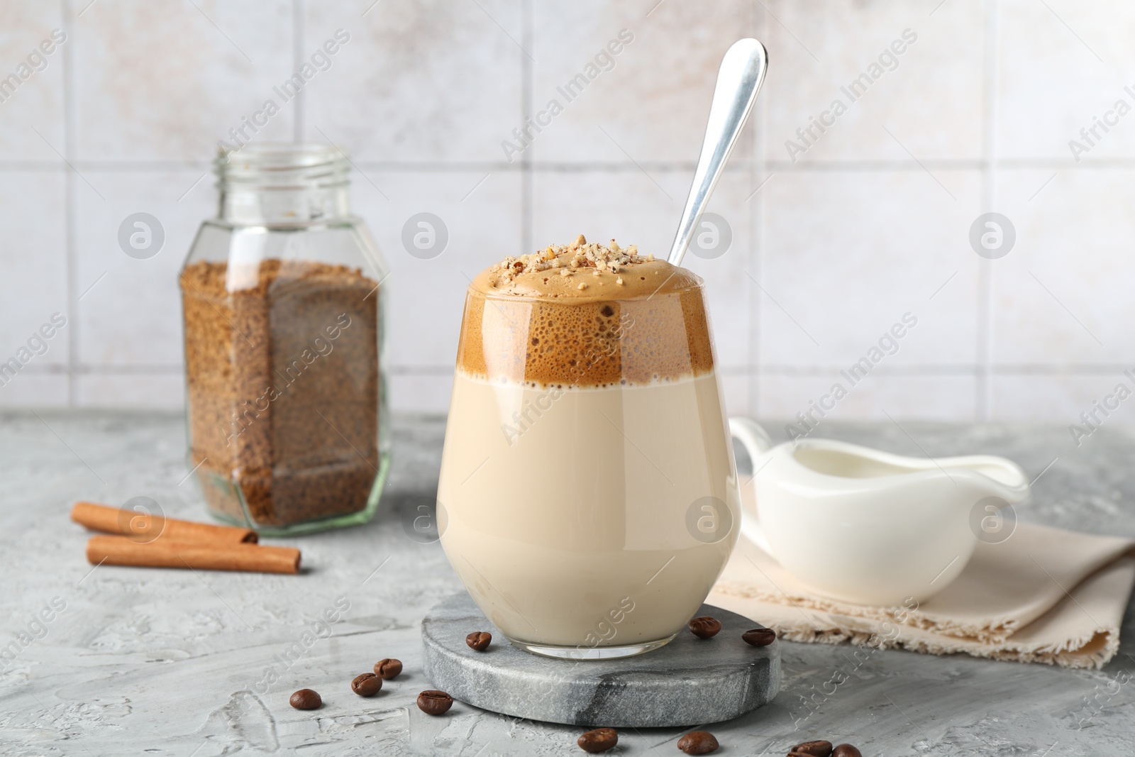 Delicious dalgona coffee in glass, beans, granules and cinnamon on grey table, closeup Photo of Delicious dalgona coffee in glass, beans, granules and cinnamon on grey table, closeup