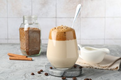 Photo of Delicious dalgona coffee in glass, beans, granules and cinnamon on grey table, closeup
