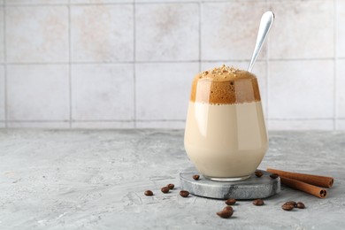Photo of Delicious dalgona coffee in glass, beans and cinnamon on grey table, space for text