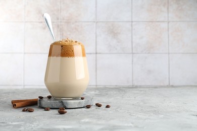 Photo of Delicious dalgona coffee in glass, beans and cinnamon on grey table, space for text