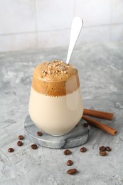 Photo of Delicious dalgona coffee in glass, beans and cinnamon on grey table, closeup