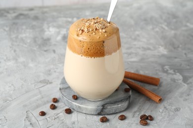 Photo of Delicious dalgona coffee in glass, beans and cinnamon on grey table, closeup