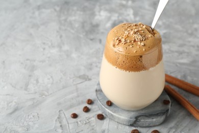 Photo of Delicious dalgona coffee in glass, beans and cinnamon on grey table, closeup. Space for text
