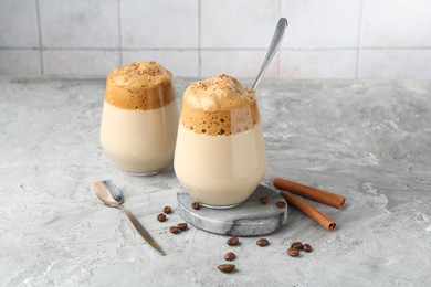 Photo of Delicious dalgona coffee in glasses, beans and cinnamon on grey table