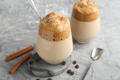 Photo of Delicious dalgona coffee in glasses, beans and cinnamon on grey table, closeup