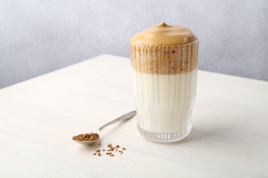Photo of Delicious dalgona coffee in glass and granules on light table, closeup. Space for text