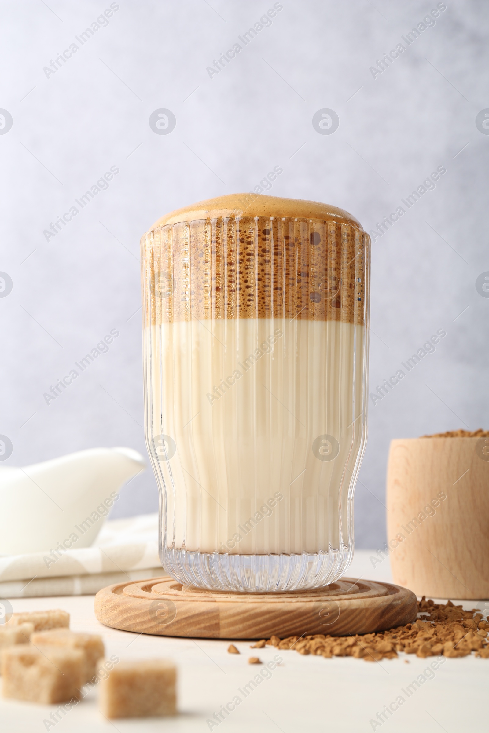 Delicious dalgona coffee in glass, granules and brown sugar on light table, low angle view Photo of Delicious dalgona coffee in glass, granules and brown sugar on light table, low angle view