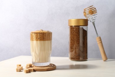 Photo of Delicious dalgona coffee in glass, brown sugar, granules and whisk on light table
