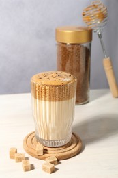 Photo of Delicious dalgona coffee in glass, brown sugar, granules and whisk on light table, closeup