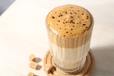 Photo of Delicious dalgona coffee in glass and brown sugar on light table, closeup. Space for text