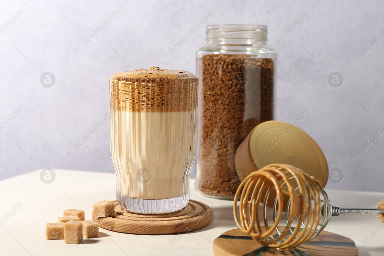 Photo of Delicious dalgona coffee in glass, whisk, brown sugar and granules on light table