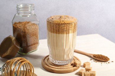 Photo of Delicious dalgona coffee in glass, whisk, brown sugar and granules on light table