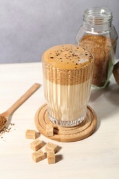 Photo of Delicious dalgona coffee in glass, brown sugar and granules on light table, closeup
