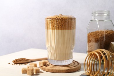 Photo of Delicious dalgona coffee in glass, whisk, brown sugar and granules on light table