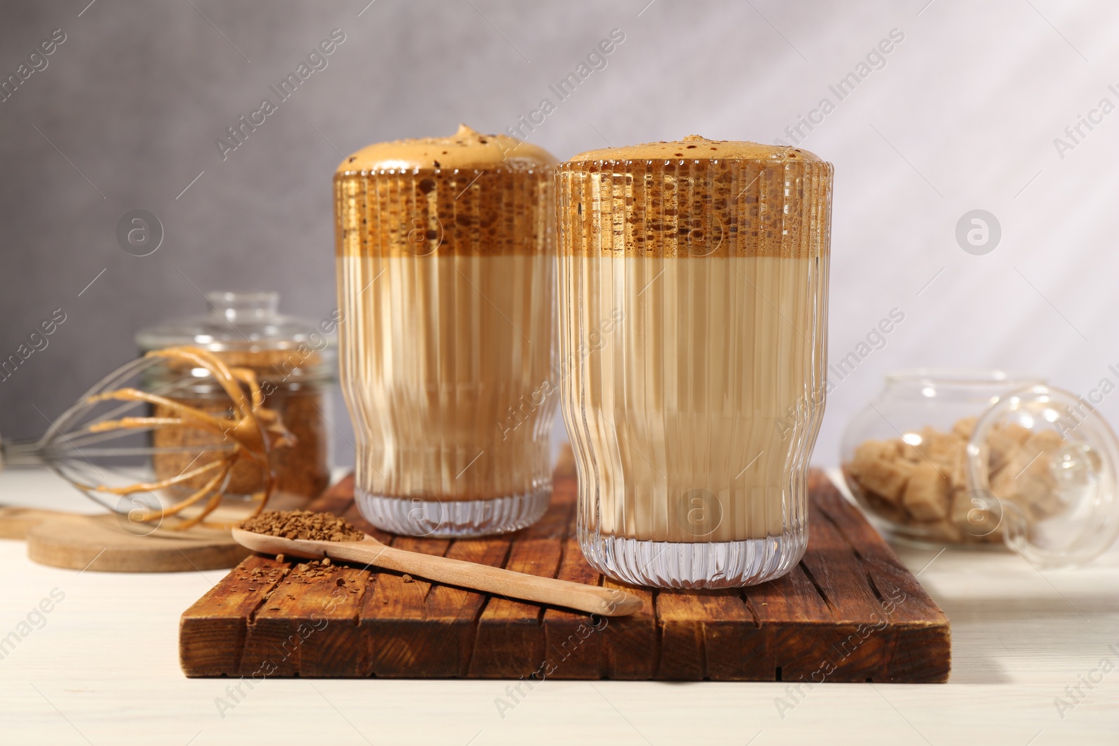 Photo of Delicious dalgona coffee in glasses, whisk, brown sugar and granules on light table, closeup