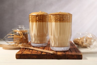 Photo of Delicious dalgona coffee in glasses, whisk, brown sugar and granules on light table, closeup