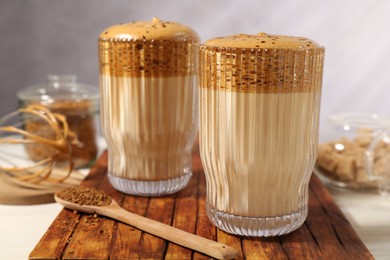 Photo of Delicious dalgona coffee in glasses, whisk, brown sugar and granules on table, closeup