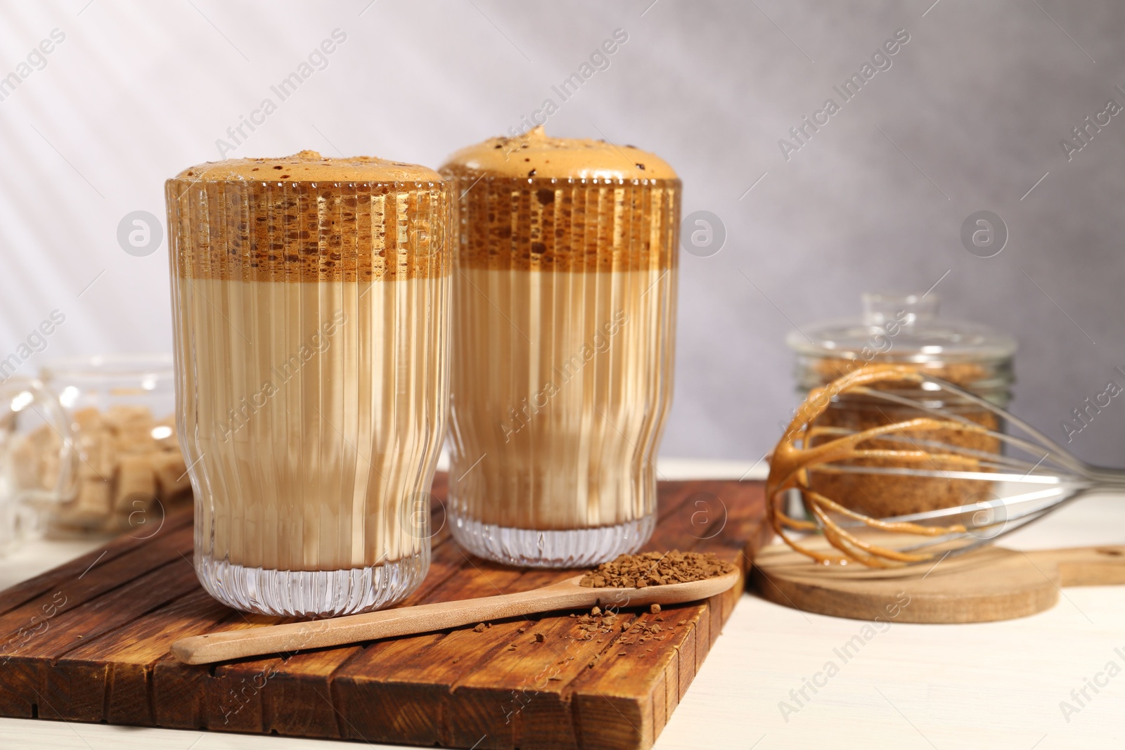 Delicious dalgona coffee in glasses, whisk, brown sugar and granules on light table, closeup Photo of Delicious dalgona coffee in glasses, whisk, brown sugar and granules on light table, closeup