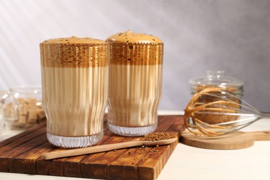 Photo of Delicious dalgona coffee in glasses, whisk, brown sugar and granules on light table, closeup