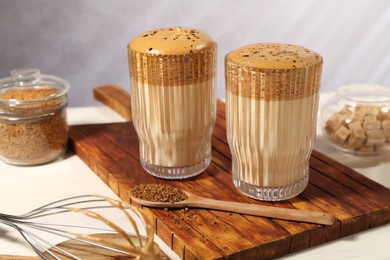 Photo of Delicious dalgona coffee in glasses, whisk, brown sugar and granules on light table, closeup